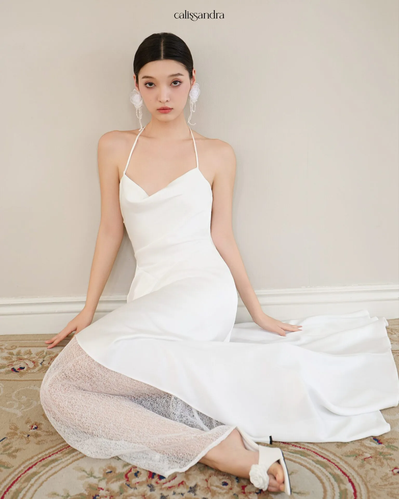 Full-length view of Opaline luxury ivory white silk satin formal evening gown, featuring a cowl halter neckline and an asymmetrical ruffled hem over delicate lace lining by Calissandra