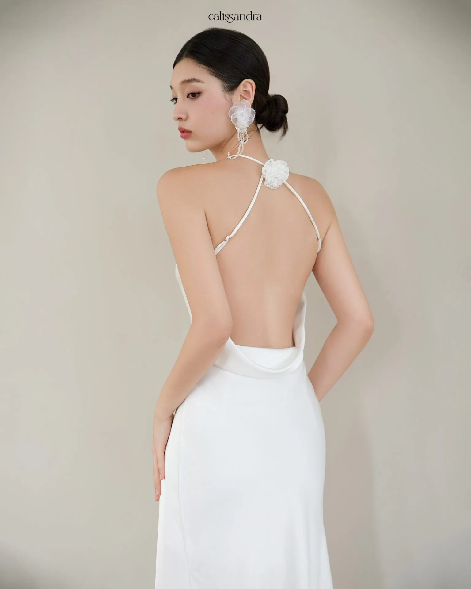 Full-length view of Opaline luxury ivory white silk satin formal evening gown, featuring a cowl halter neckline and an asymmetrical ruffled hem over delicate lace lining by Calissandra
