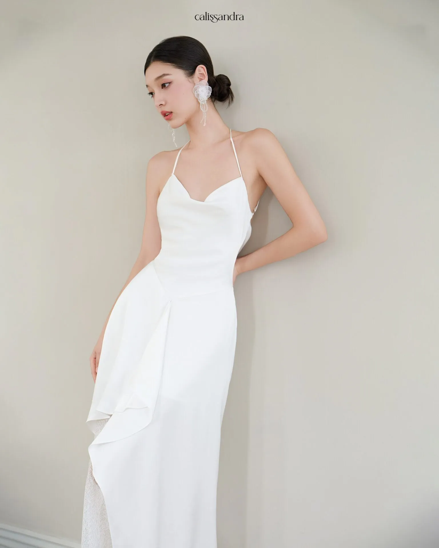 Full-length view of Opaline luxury ivory white silk satin formal evening gown, featuring a cowl halter neckline and an asymmetrical ruffled hem over delicate lace lining by Calissandra