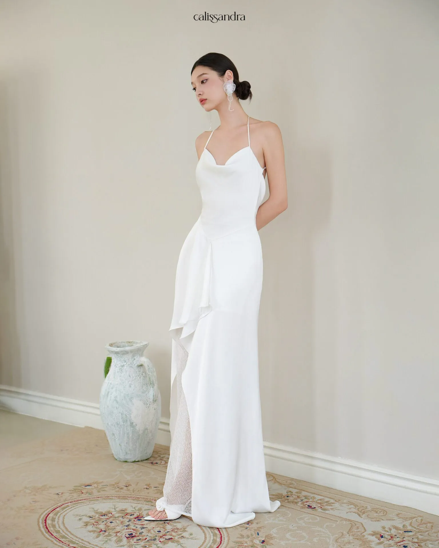 Full-length view of Opaline luxury ivory white silk satin formal evening gown, featuring a cowl halter neckline and an asymmetrical ruffled hem over delicate lace lining by Calissandra