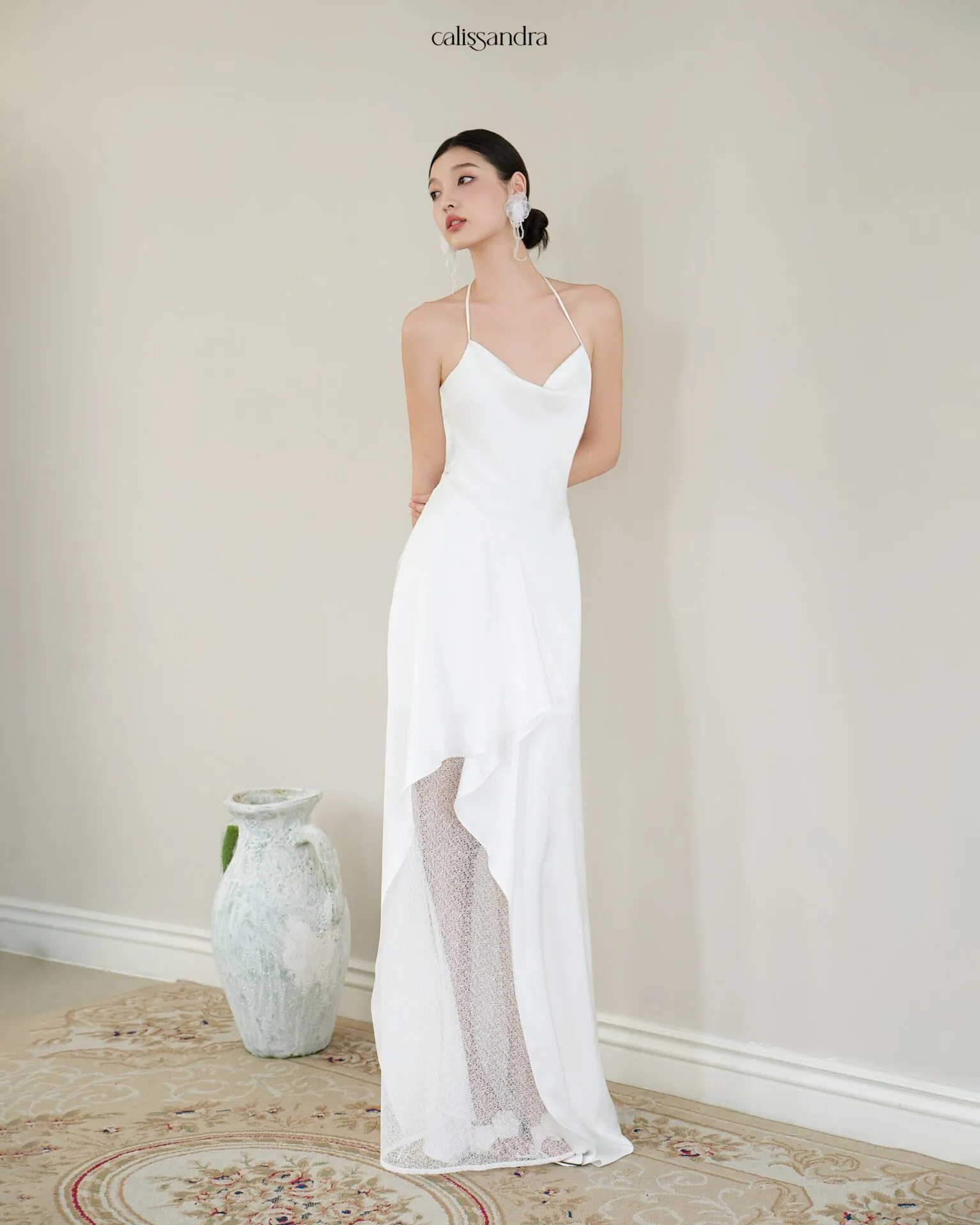 Full-length view of Opaline luxury ivory white silk satin formal evening gown, featuring a cowl halter neckline and an asymmetrical ruffled hem over delicate lace lining by Calissandra
