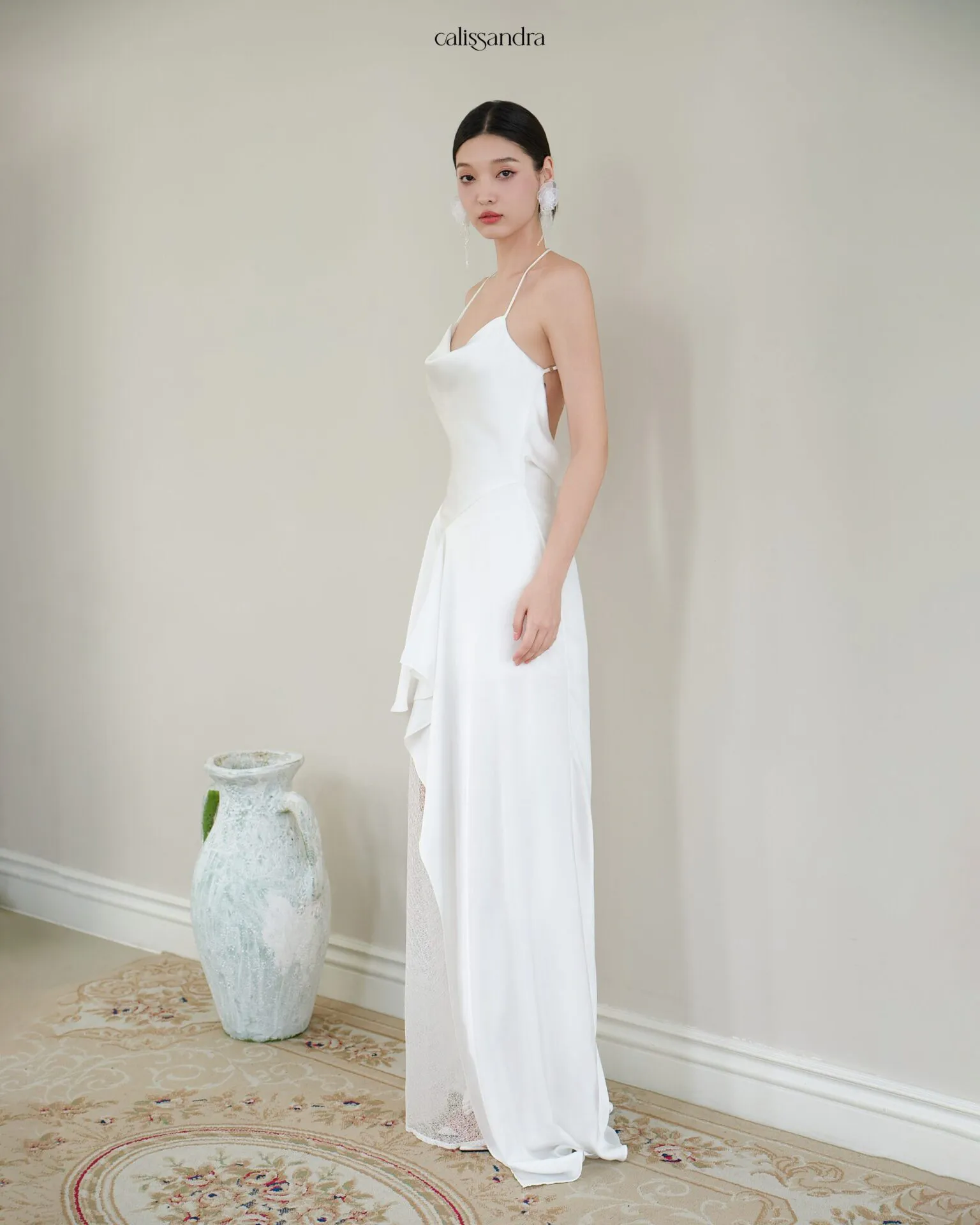 Full-length view of Opaline luxury ivory white silk satin formal evening gown, featuring a cowl halter neckline and an asymmetrical ruffled hem over delicate lace lining by Calissandra