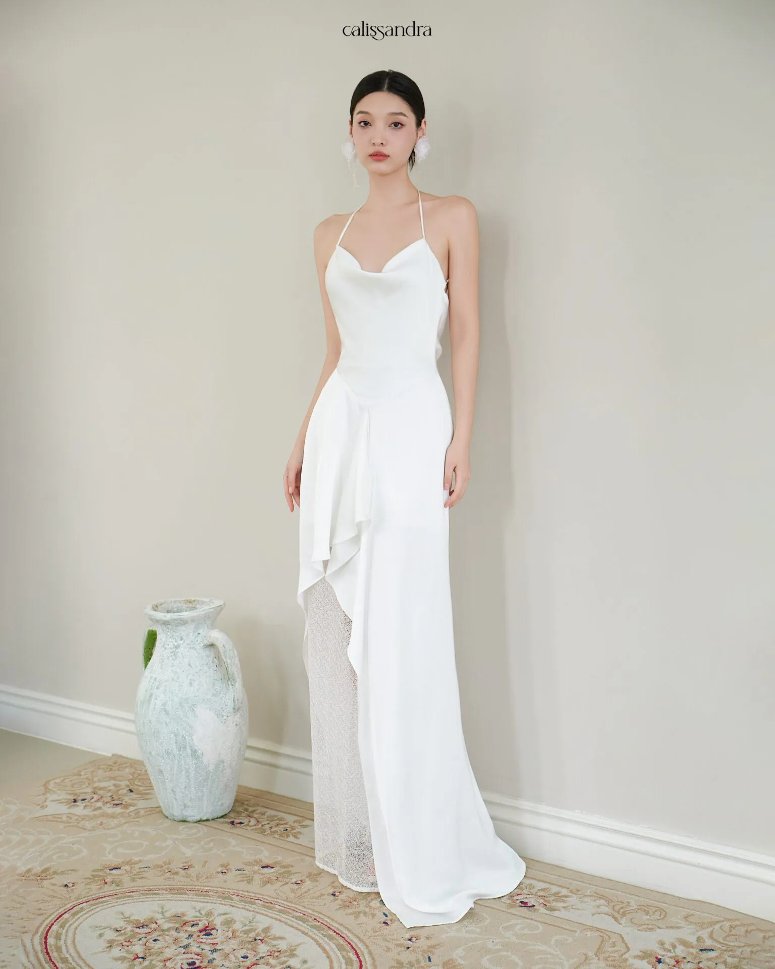 Full-length view of Opaline luxury ivory white silk satin formal evening gown, featuring a cowl halter neckline and an asymmetrical ruffled hem over delicate lace lining by Calissandra