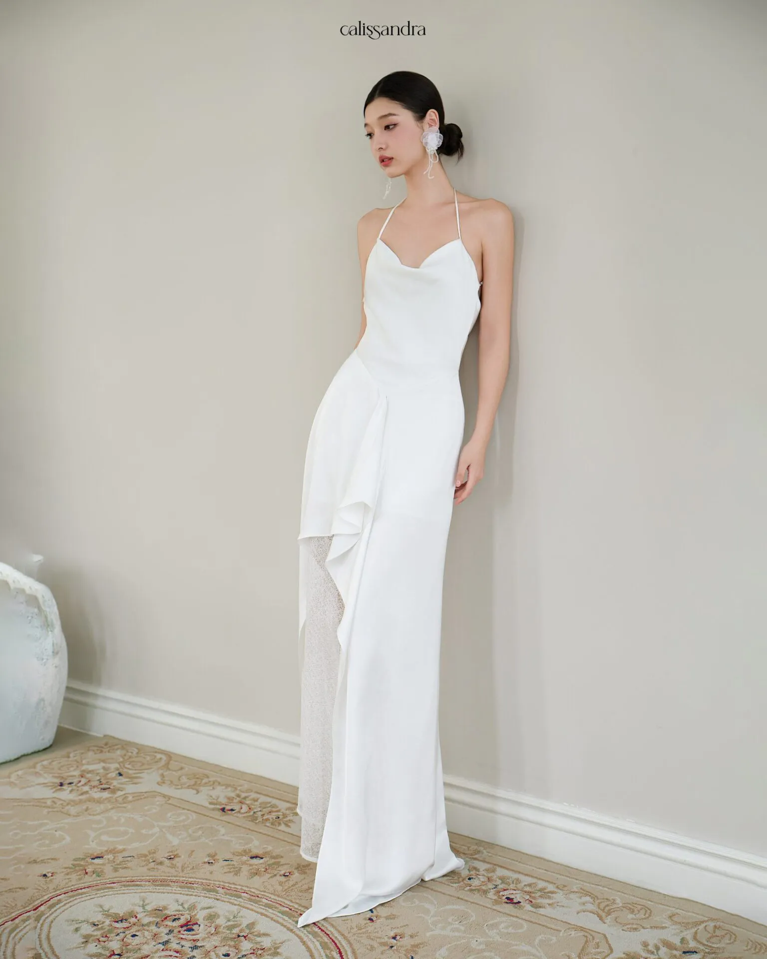 Full-length view of Opaline luxury ivory white silk satin formal evening gown, featuring a cowl halter neckline and an asymmetrical ruffled hem over delicate lace lining by Calissandra