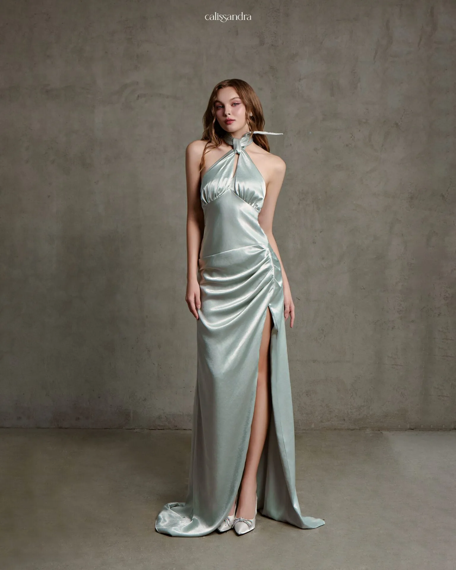 Full-length view of Jolivie luxury metallic silver-green silk satin evening gown, featuring a keyhole halter neck, a ruched bodice, and a high side slit by Calissandra