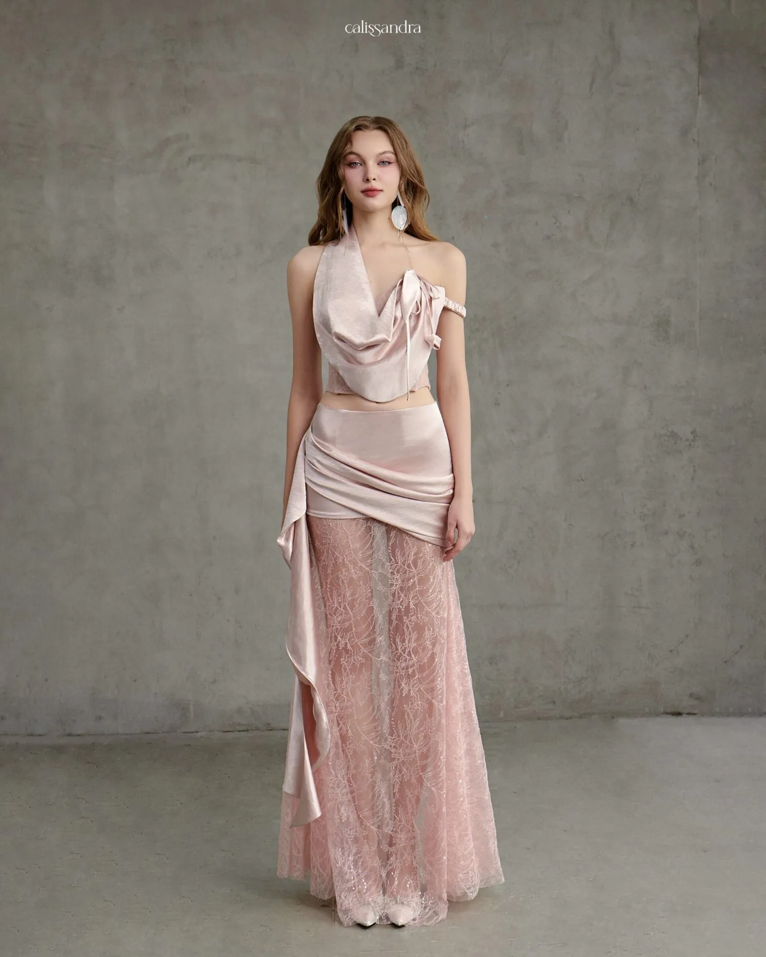 Full-length view of Miralys luxury blush pink two-piece set, featuring an asymmetrical cowl corset top and a draped satin maxi skirt with a sheer embroidered lace overlay by Calissandra