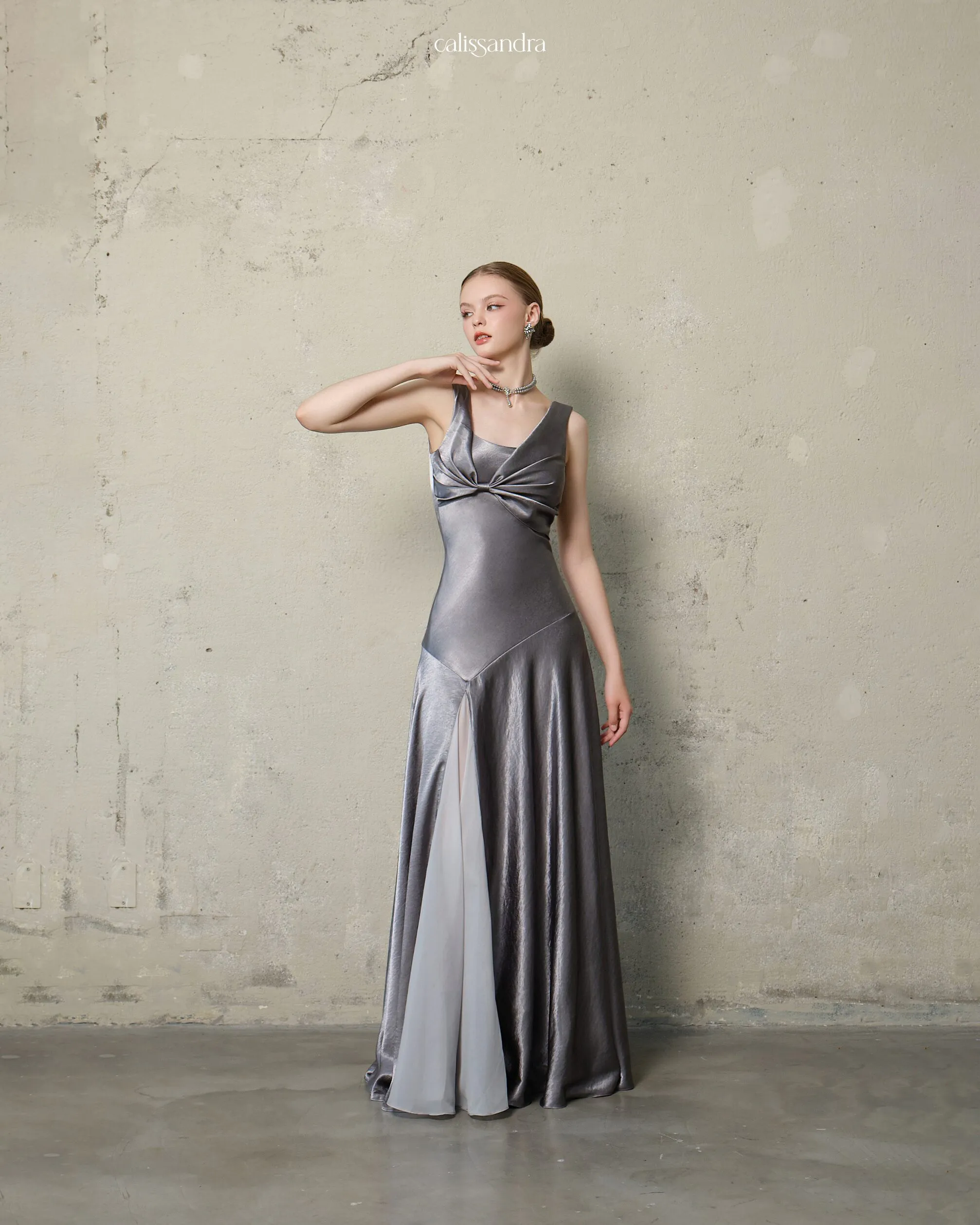 Full-length view of Marceline luxury metallic silver gray silk satin evening gown, featuring a twisted front bodice and a high slit detailed with a sheer chiffon insert by Calissandra