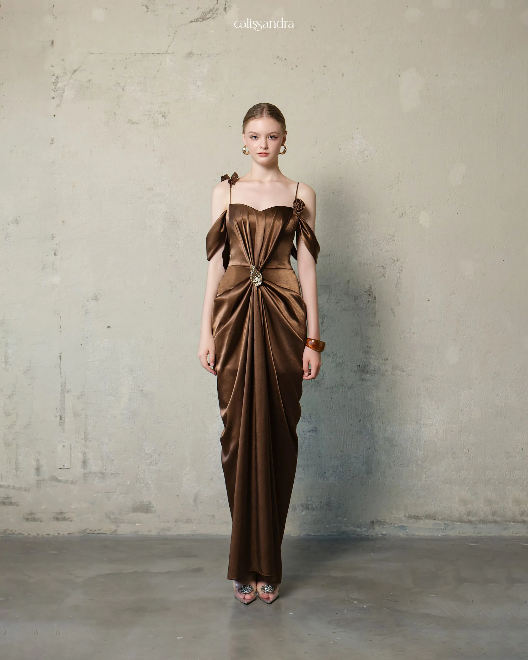 Full-length view of Velmora luxury chocolate brown silk satin evening gown, featuring a cold-shoulder sweetheart neckline, 3D rose accents, and a central gold brooch detailing by Calissandra