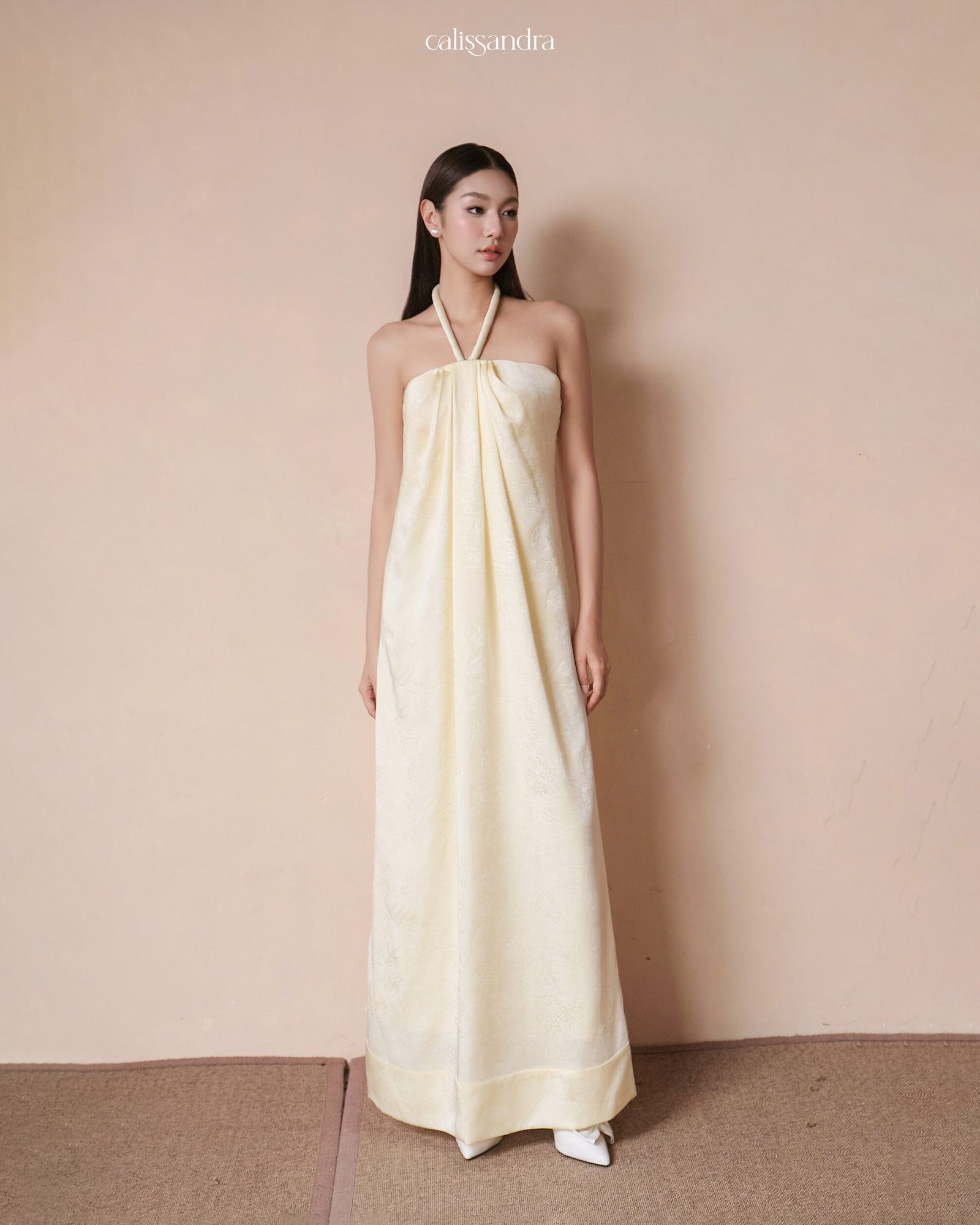 Full-length front view of Doralia cream silk maxi dress styled with a thin halter neck strap and loose pleated strapless bodice by Calissandra